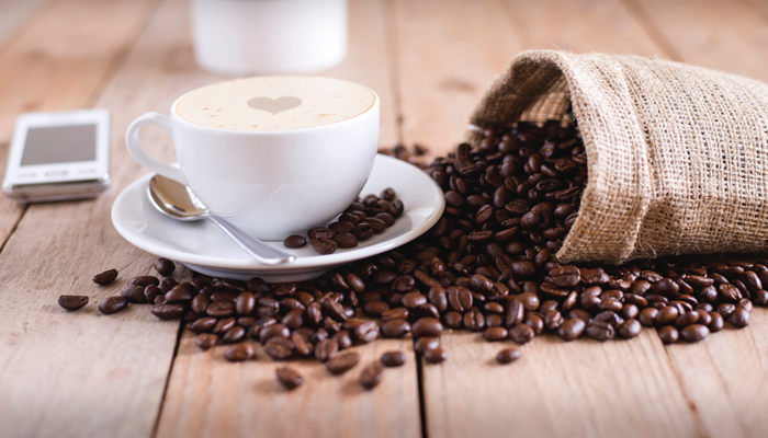 Café em uma xícara ao lado de um sementes de café sobre a mesa.